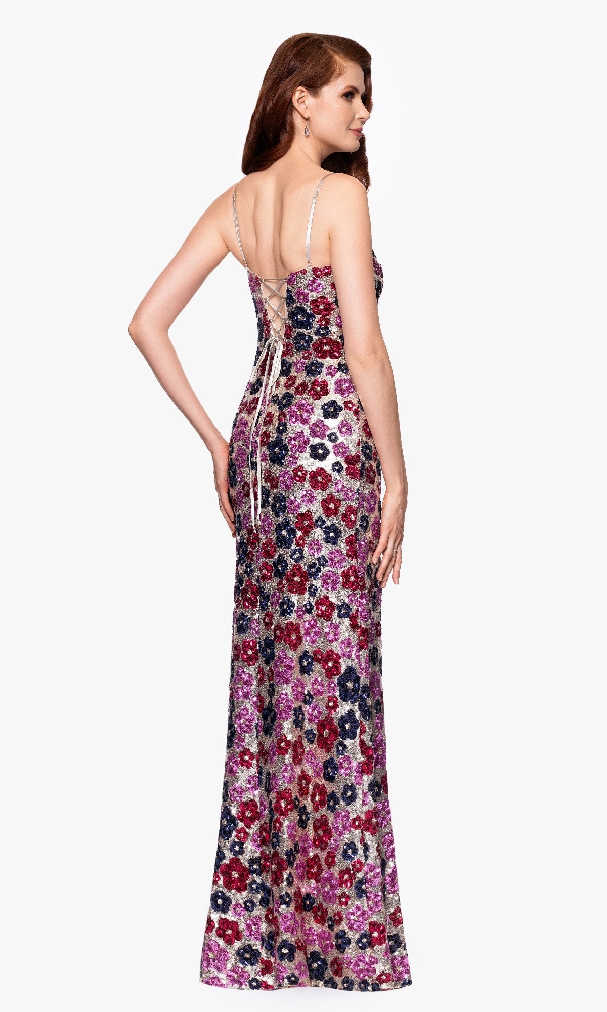 A woman faces away, wearing the Betsy & Adam A27017 Floral-Sequin Long Prom Dress with thin straps and lace-up back detail.